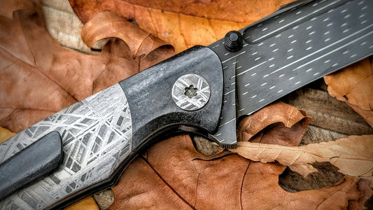 Custom folding knife with etched meteorite handle and pivot, dark bolster and patterned blade